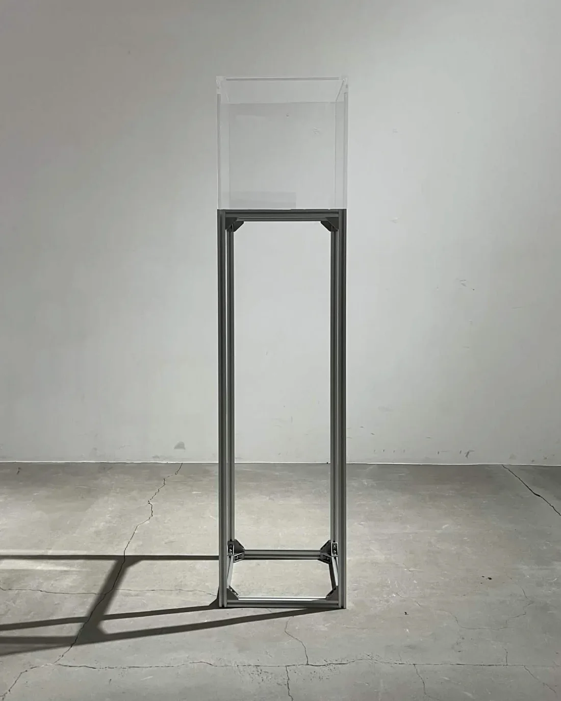 Quietus Machine: a transparent acrylic cube on a slender aluminium stand in a bare grey room